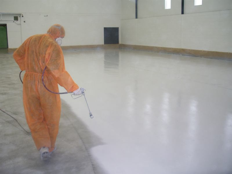 Applicator spraying epoxy coating across a commercial floor