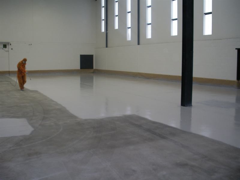 Applicator spray-applying water-based epoxy across a large warehouse floor