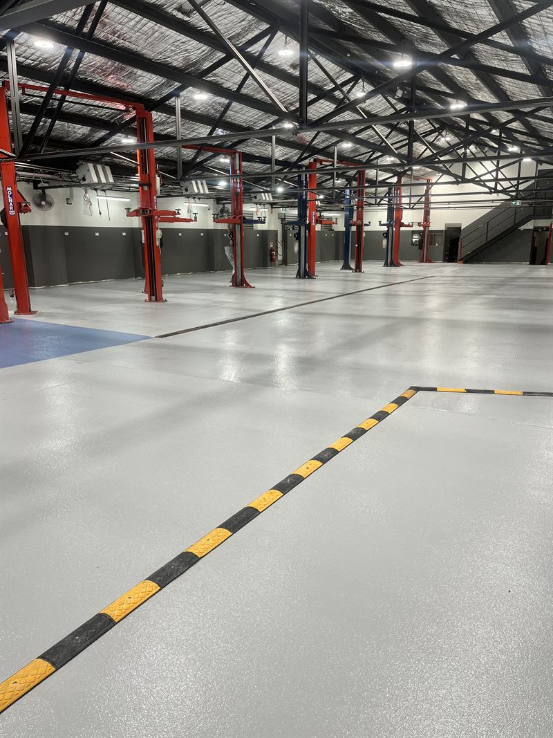 Light grey workshop floor with yellow and black walkway lines between the vehicle hoists